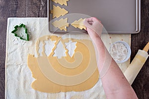 WomanÃ¢â¬â¢s hands cutting out Christmas tree sugar cookies, pastry cloth, cookie sheet